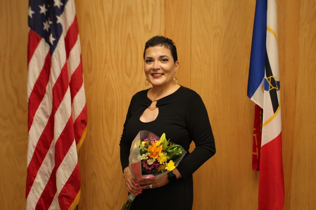 Alicia Morales, Joliet Township Government Supervisor, holding flowers, standing between the American flag and the Joliet Township flag